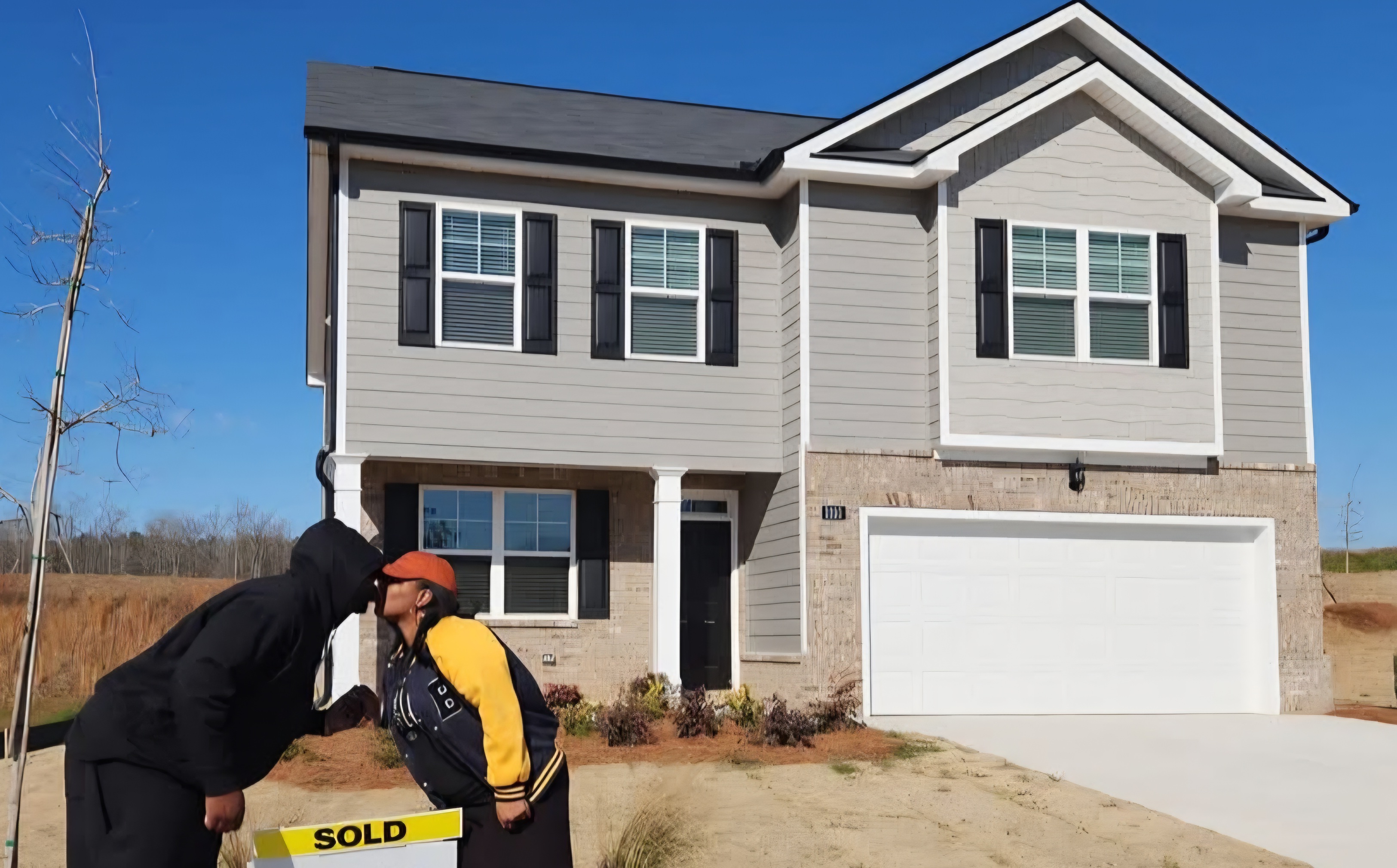 Happy clients celebrating in front of their new home with a SOLD sign